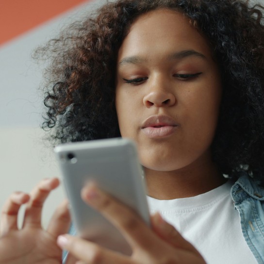 Een lachende jongen met een telefoon in zijn hand met een spijkerblouse.